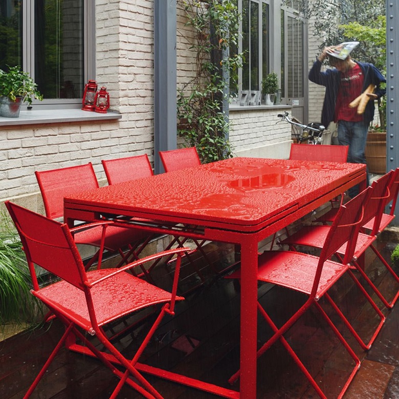 Red Biarritz dining table by Fermob outside in a garden while raining