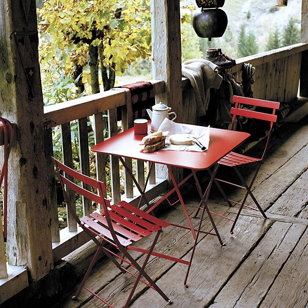 Breakfast laid out on a veranda with a red Fermob table and two chairs