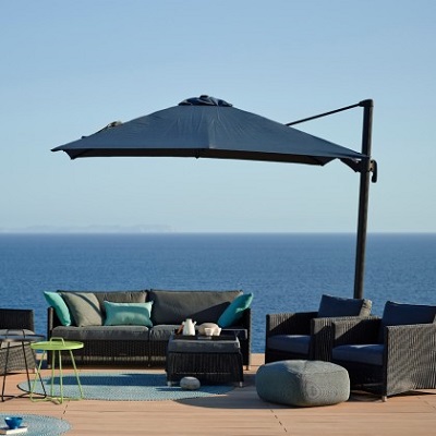 The Hyde hanging parasol by Cane-Line, with outdoor furniture and an oceanview background 